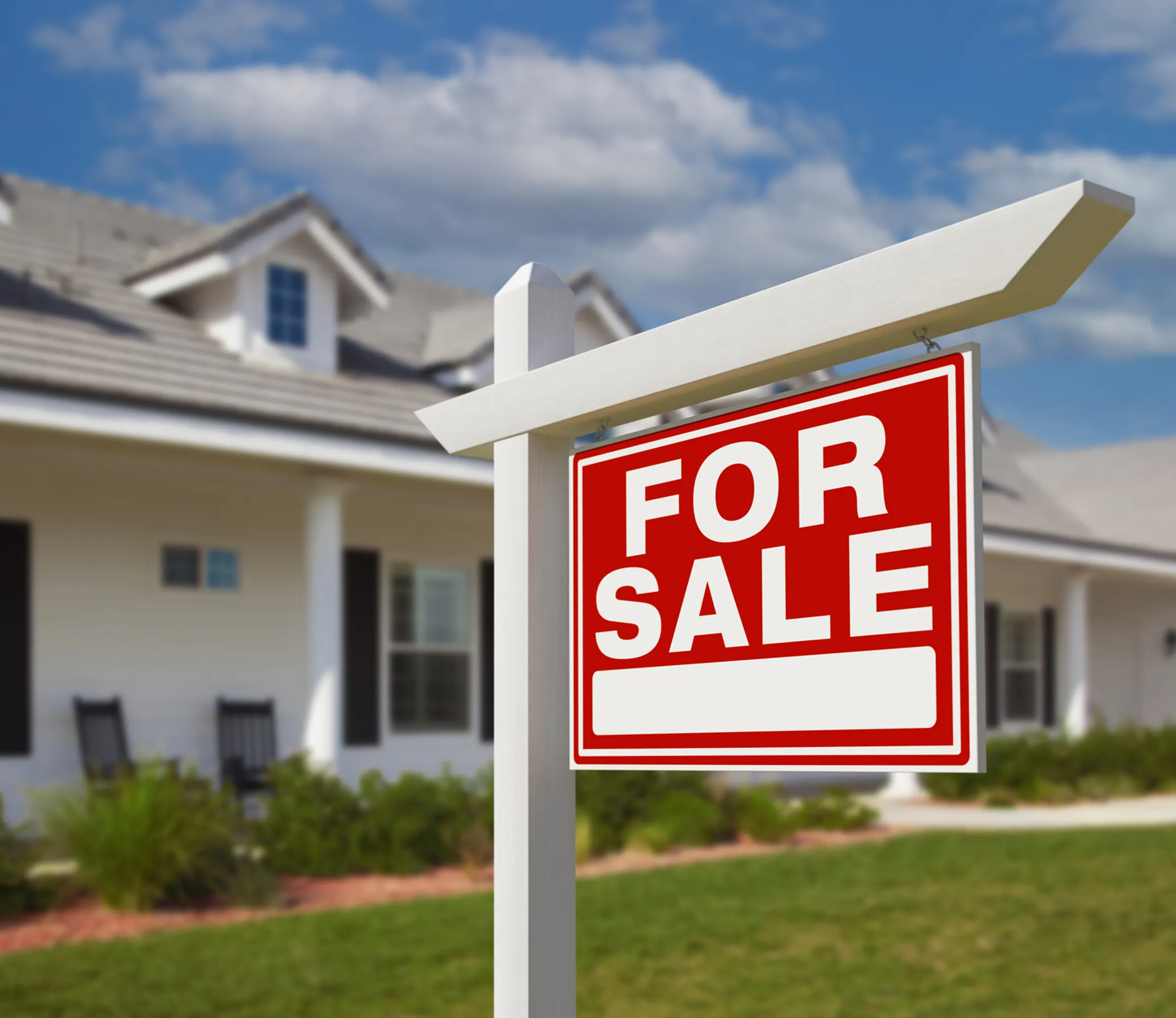 Red "For Sale" sign in front of a suburban house with a lawn and a cloudy sky in the background.