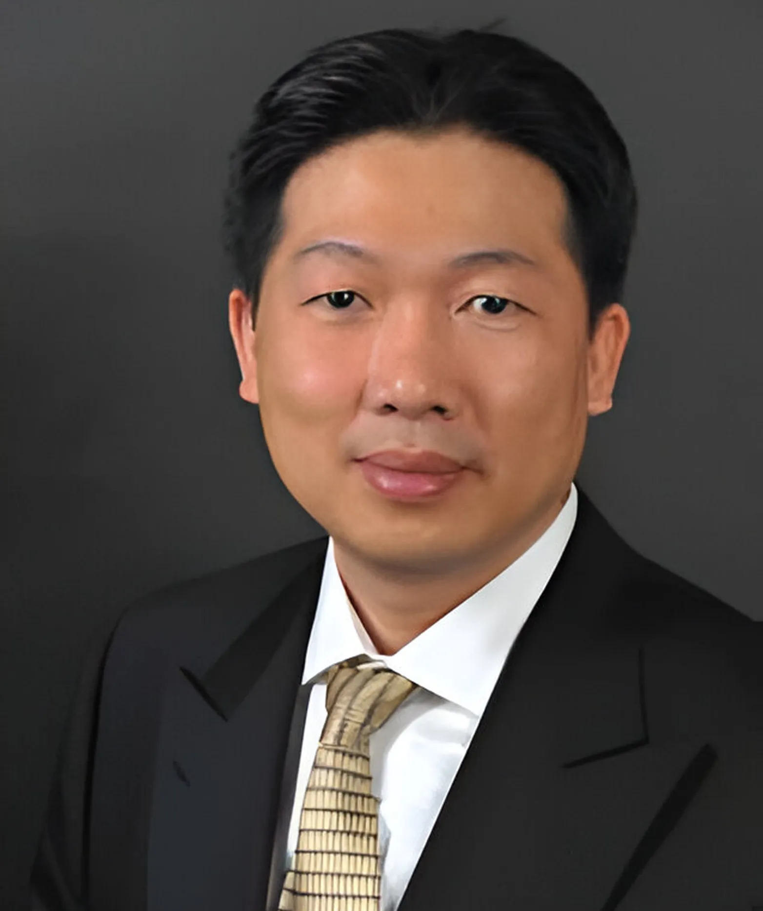 A man in a suit and tie poses against a dark backdrop with a neutral expression.